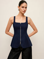 A zip-up denim peplum blouse with wide straps and stylish waist detail, paired with dark pants.