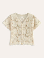 A cropped cream knit cardigan with floral crochet designs, short sleeves, v-neck, button-up front.