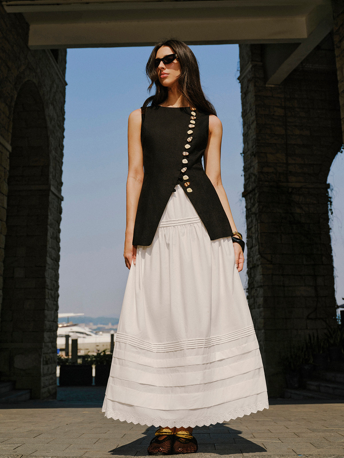 A linen vest with elegant button details styled with a long, pleated white skirt.