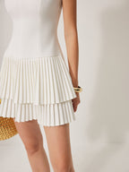 Sleeveless white mini dress with square neckline, fitted bodice, pleated detail, and layered skirt.