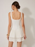 A sleeveless, mini-length square neckline dress with a fitted bodice and tiered pleated skirt.