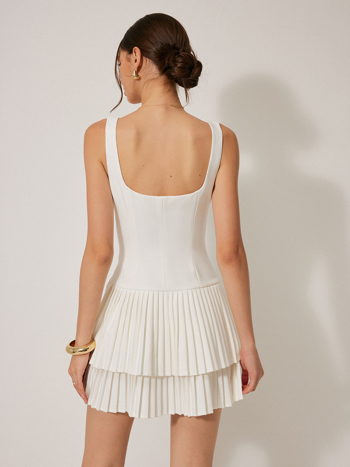 A sleeveless, mini-length square neckline dress with a fitted bodice and tiered pleated skirt.