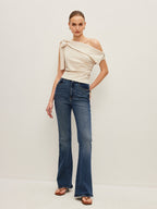 One-shoulder blouse with elegant bow detail, blue high-waisted flare jeans, brown sandals.