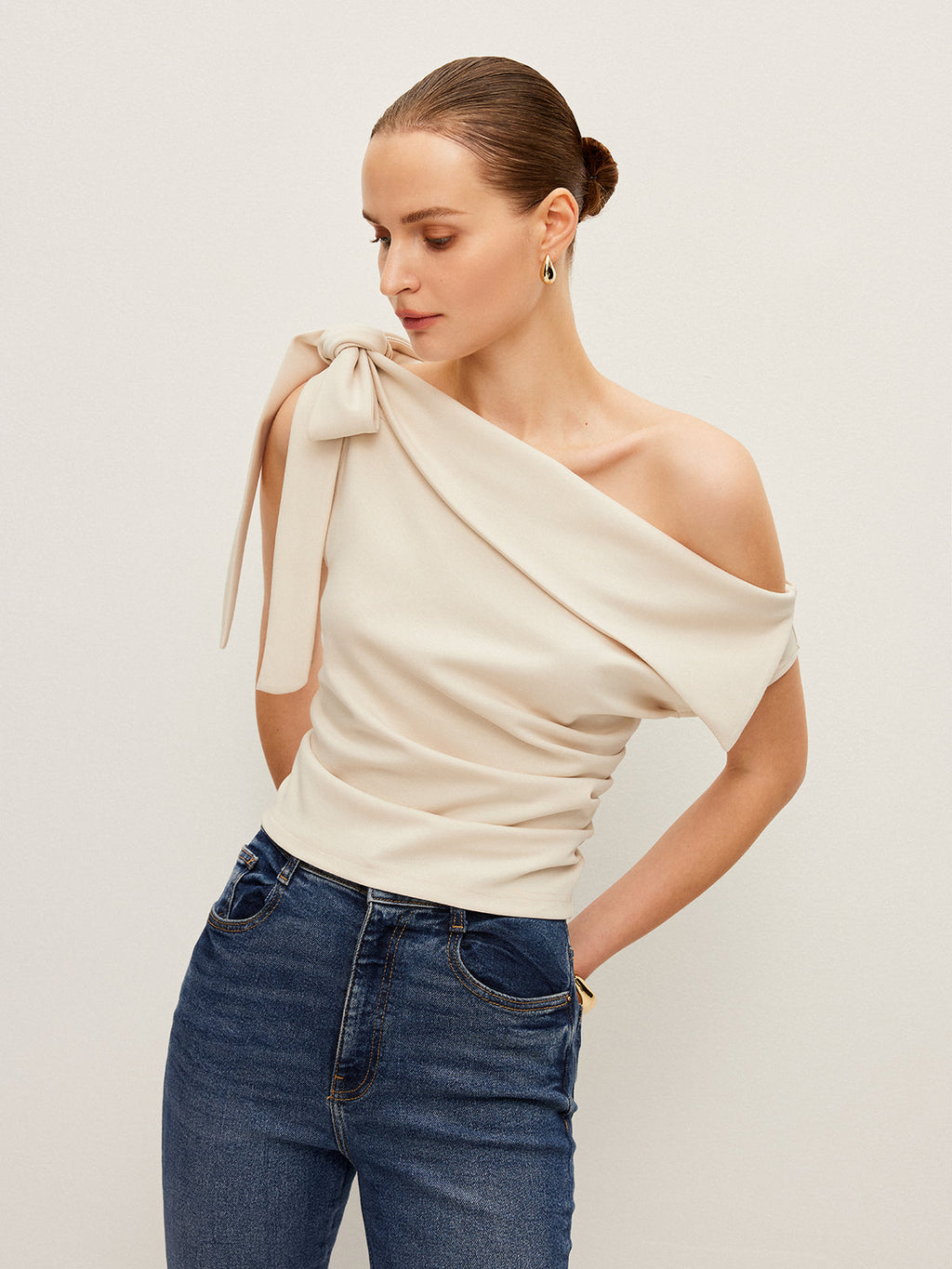 A LA FINE FLEUR one-shoulder blouse with an elegant bow detail and blue jeans.