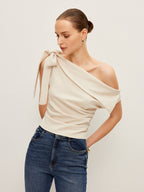 A LA FINE FLEUR one-shoulder blouse with an elegant bow detail and blue jeans.