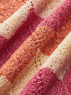 Close-up of a knit halter dress with cream, pink, red, and orange striped panels.
