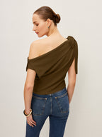 Olive green one-shoulder blouse with elegant bow detail, paired with blue jeans.