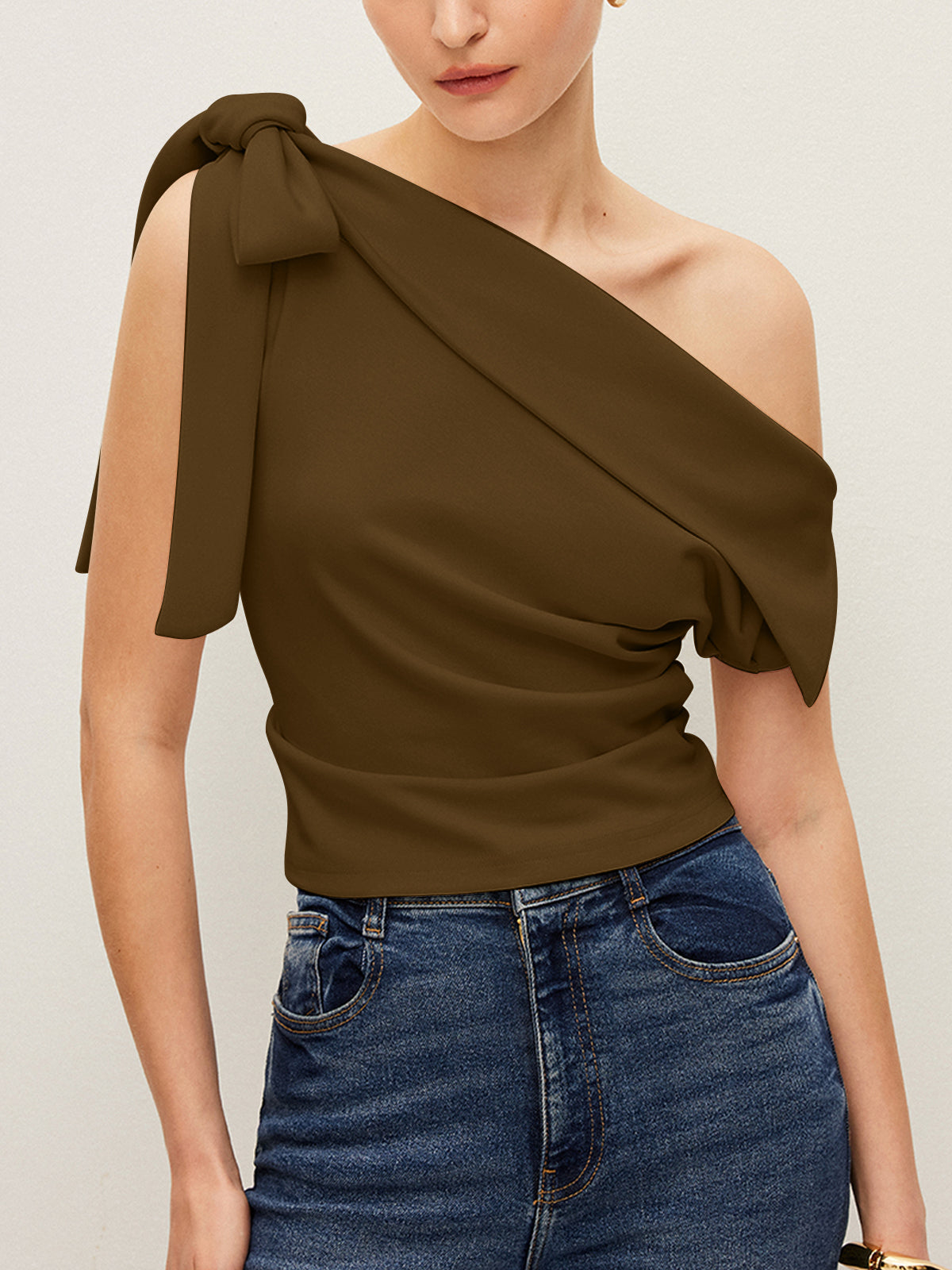 The LA FINE FLEUR one-shoulder blouse with elegant bow, styled with high-waisted blue jeans.