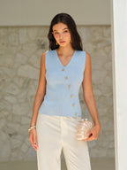 A V-neck sleeveless knit top with gold buttons, paired with white pants.