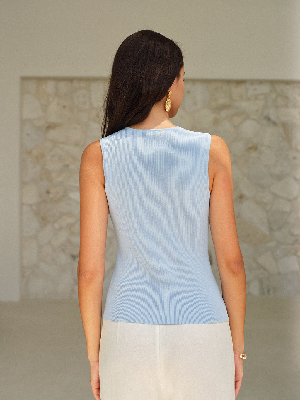 Light blue knit V-neck sleeveless top with elegant gold buttons and cream pants.