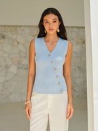 Light blue BYPINKYPARIS V-neck sleeveless top with elegant gold buttons, paired with cream pants.