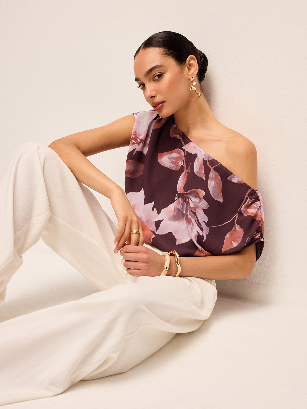 LA FINE FLEUR Floral One-Shoulder Blouse with Belt Detail and white wide-leg pants.