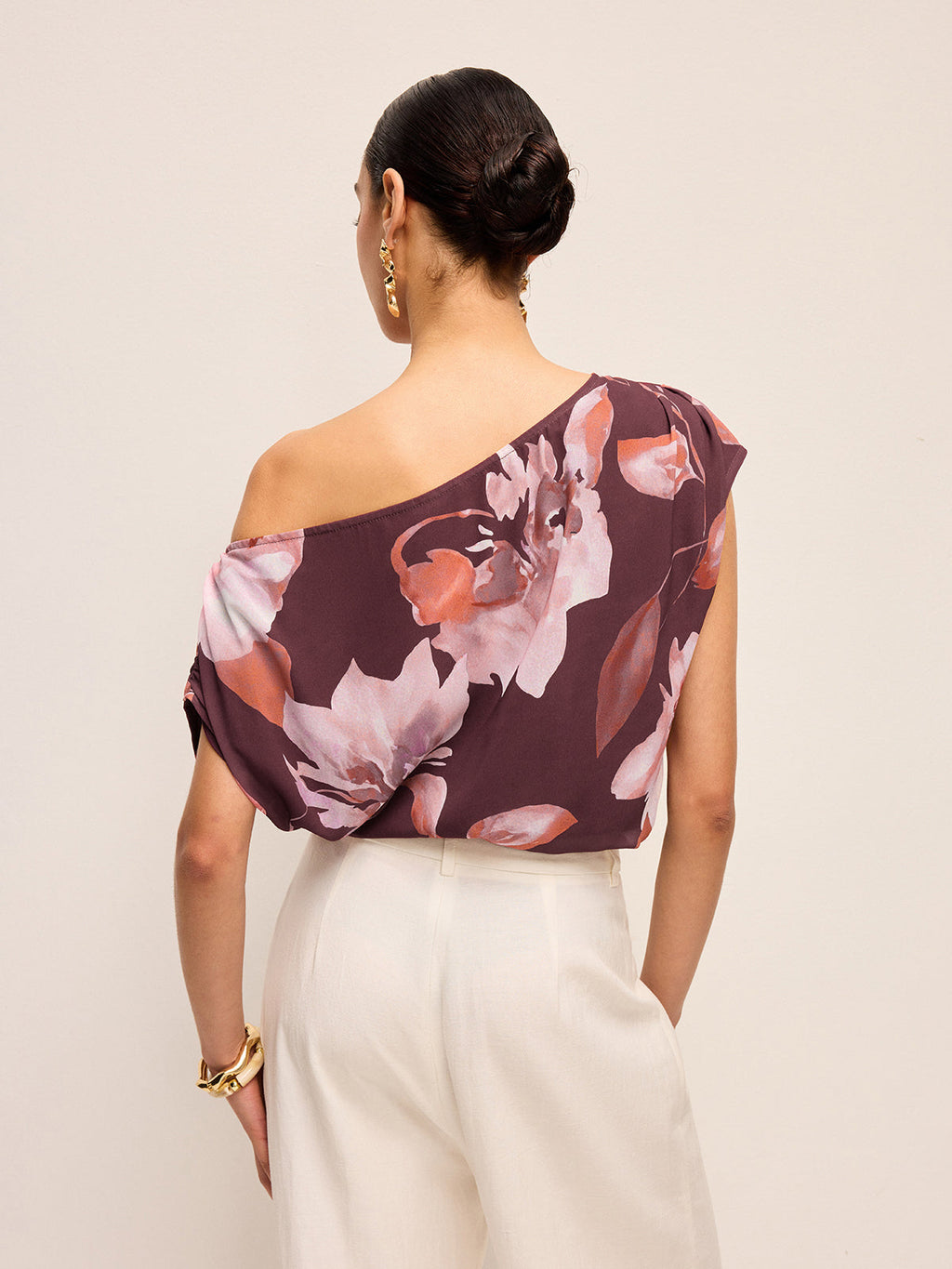 Floral one-shoulder blouse with belt detail paired with white high-waisted pants.