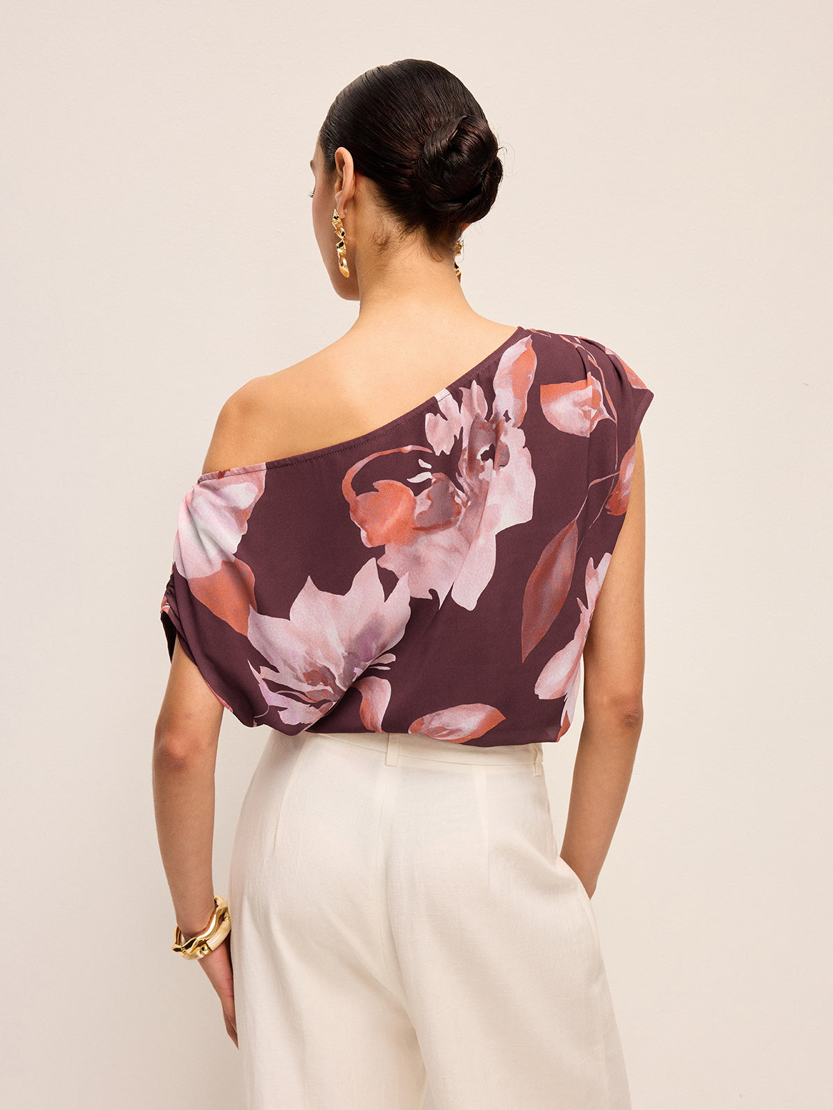 Floral one-shoulder blouse with belt detail paired with white high-waisted pants.