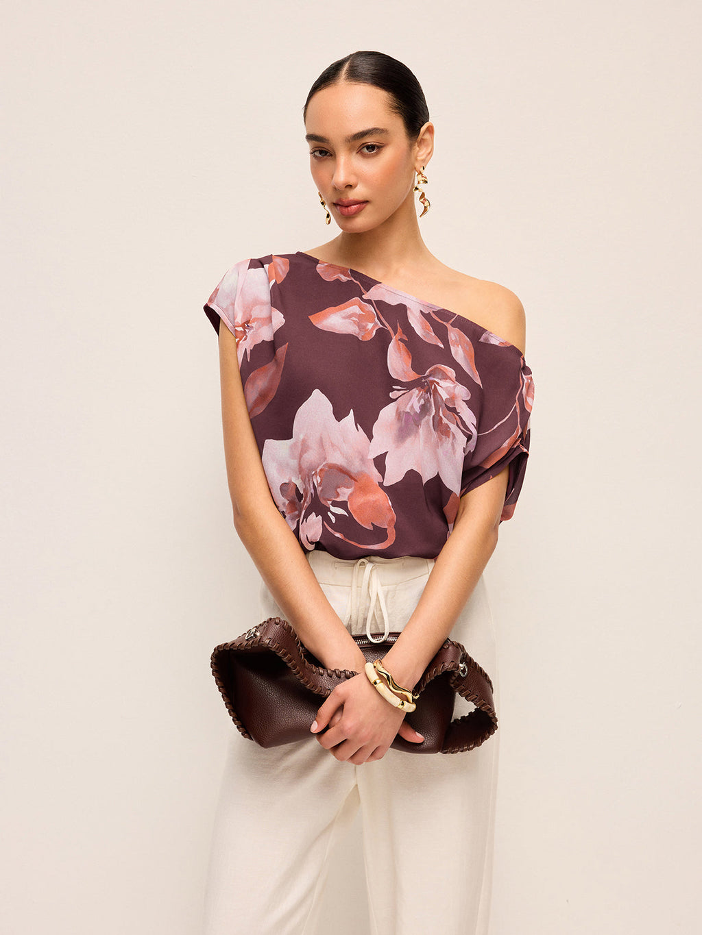 LA FINE FLEUR’s floral one-shoulder blouse with belt detail paired with beige pants.
