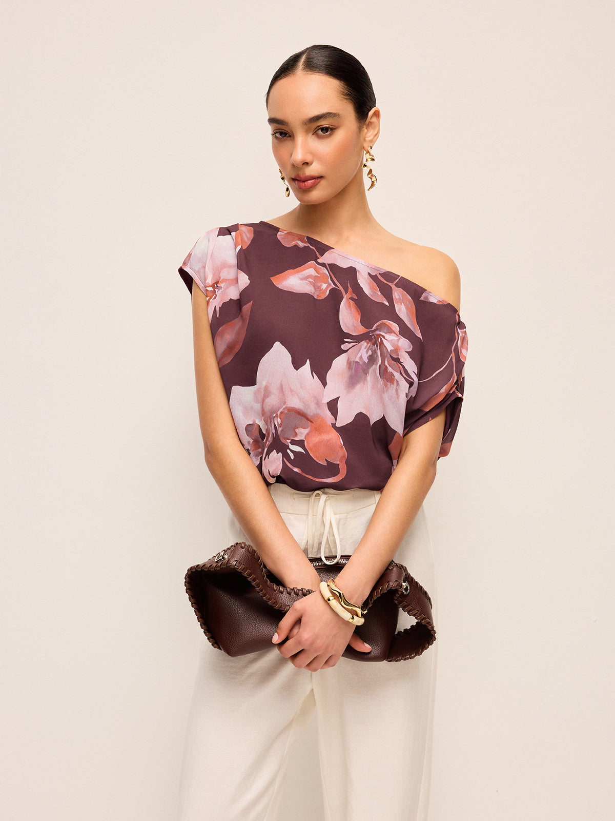 LA FINE FLEUR’s floral one-shoulder blouse with belt detail paired with beige pants.