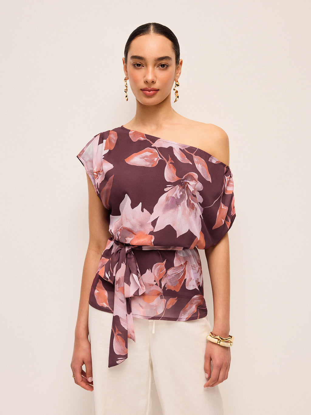 LA FINE FLEUR Floral One-Shoulder Blouse with Belt Detail, styled with white pants.