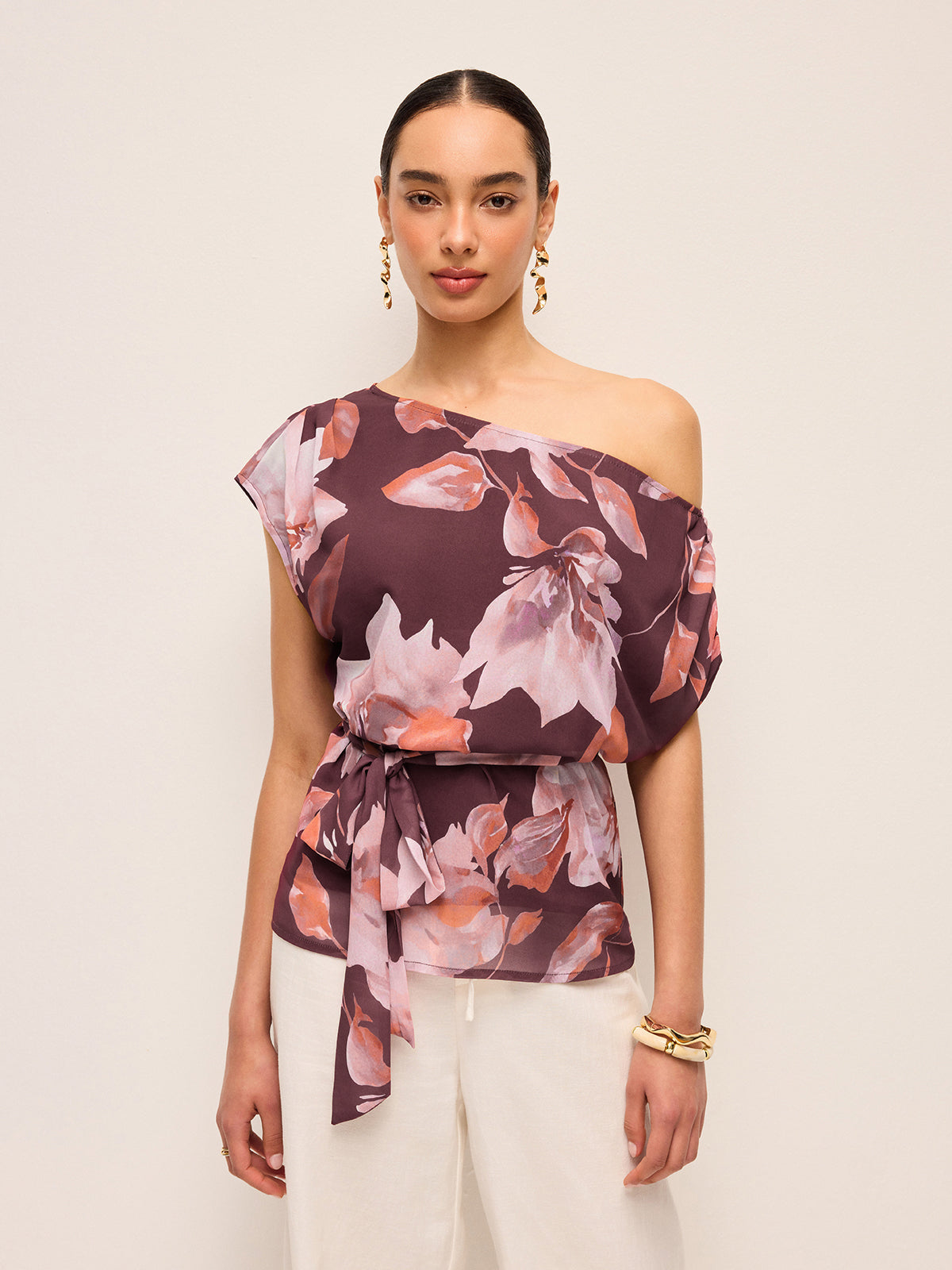 LA FINE FLEUR Floral One-Shoulder Blouse with Belt Detail, styled with white pants.