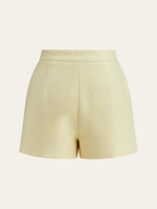 High-waisted light yellow tweed shorts with front pleats and pearl-button detailing.
