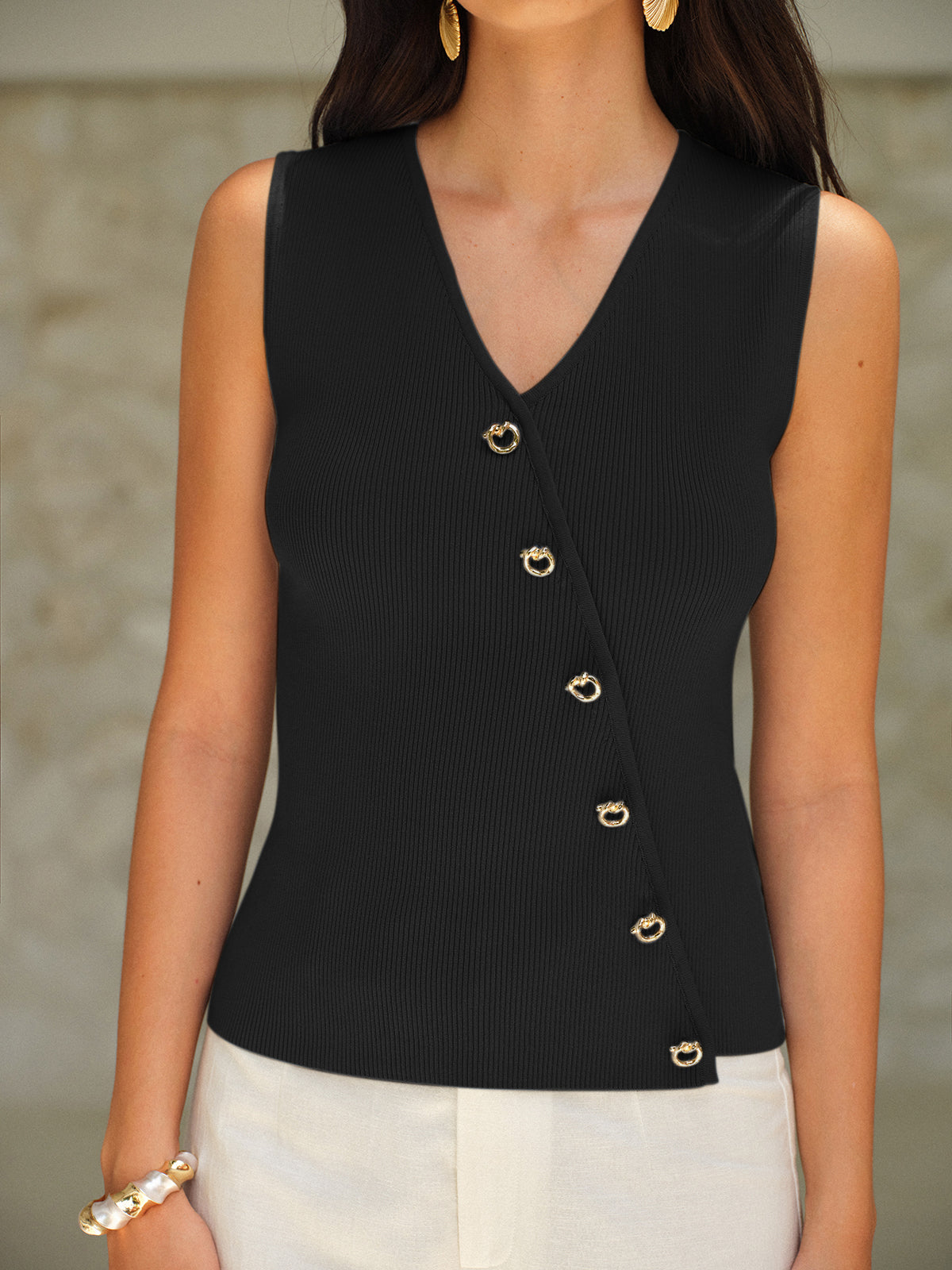 Black ribbed soft knit V-neck sleeveless top with elegant gold buttons and white pants.