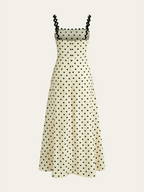 Cream midi dress with black square dots, scalloped straps, buttoned bodice, and flared skirt.