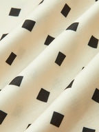 A cream midi dress with black polka dots, scalloped straps, and softly pleated skirt.