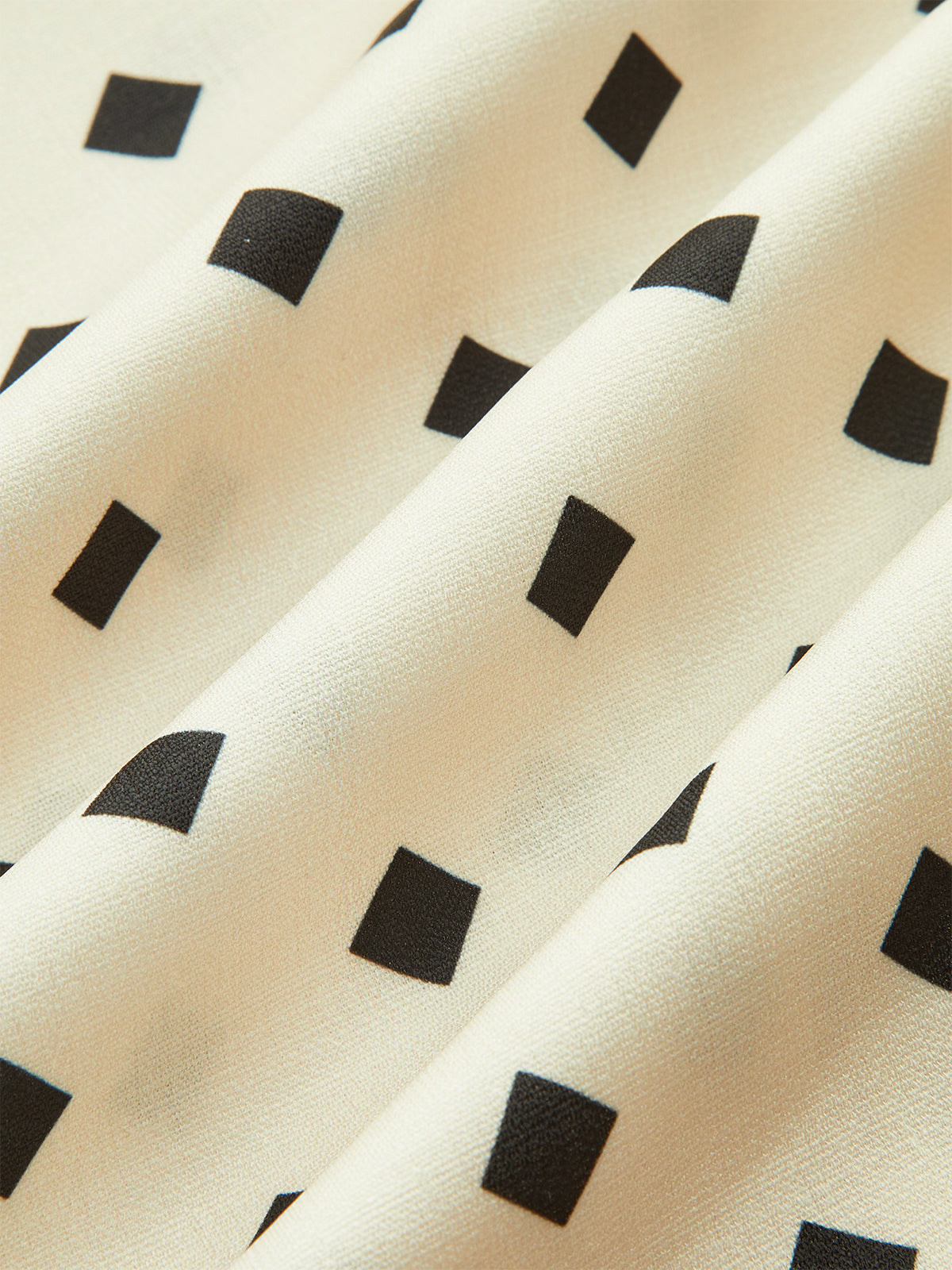 A cream midi dress with black polka dots, scalloped straps, and softly pleated skirt.