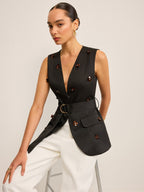 Black sleeveless sequin floral vest with deep V-neck, gold buckle, and white high-waisted pants.