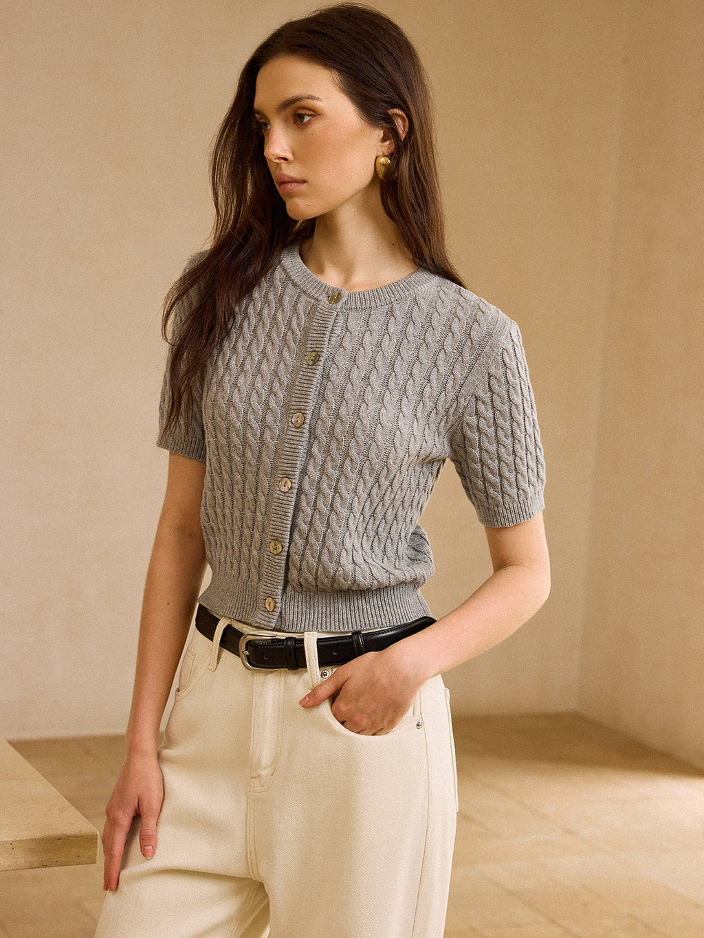 Short-sleeve cable knit cardigan sweater with cream wide-leg trousers and black leather belt.
