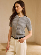 Short-sleeve cable knit cardigan sweater with cream wide-leg trousers and black leather belt.