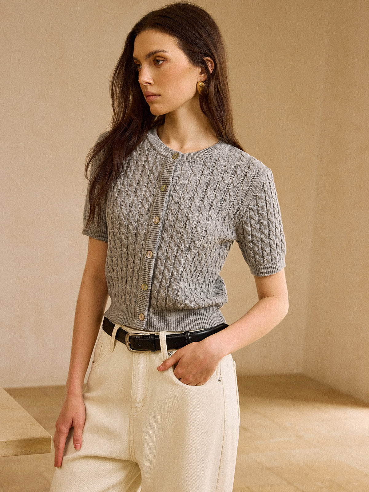 Short-sleeve cable knit cardigan sweater with cream wide-leg trousers and black leather belt.