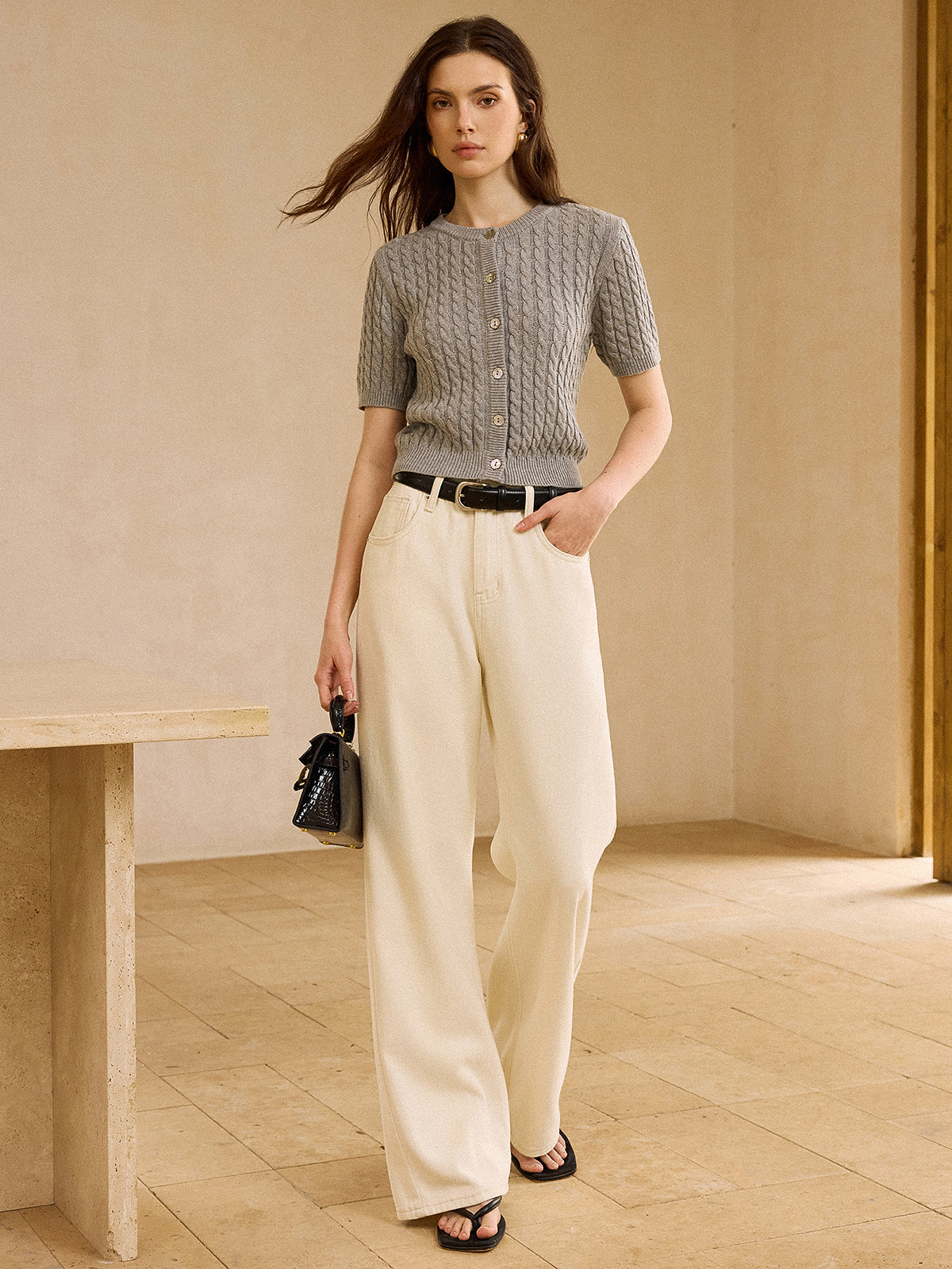 LA FINE FLEUR short-sleeve cable knit cardigan sweater with cream wide-leg pants and black belt.