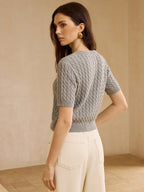 Short-sleeve cable knit cardigan sweater styled with high-waisted off-white pants.