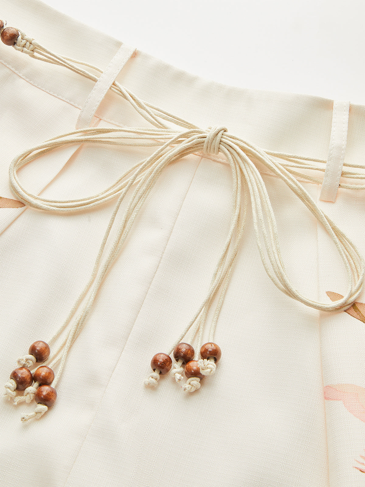 Light beige LA FINE FLEUR mid-waist shorts with tropical belt, wooden beads, macrame ties.