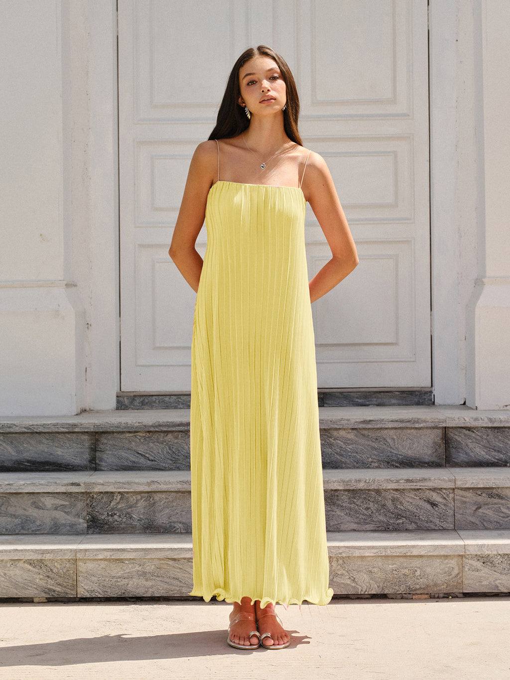 A sleeveless yellow maxi dress with thin spaghetti straps and graceful, flowing pleats.