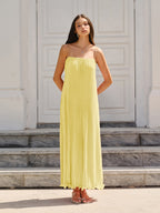 A sleeveless yellow maxi dress with thin spaghetti straps and graceful, flowing pleats.
