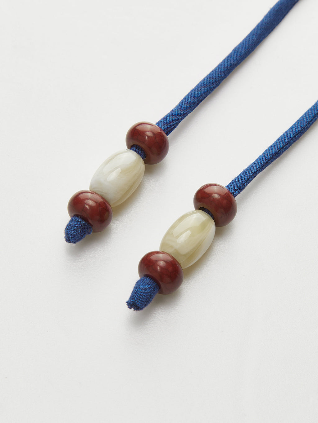 Asymmetric sleeveless top with blue wrap-tie cords, reddish-brown beads, and a cream bead.