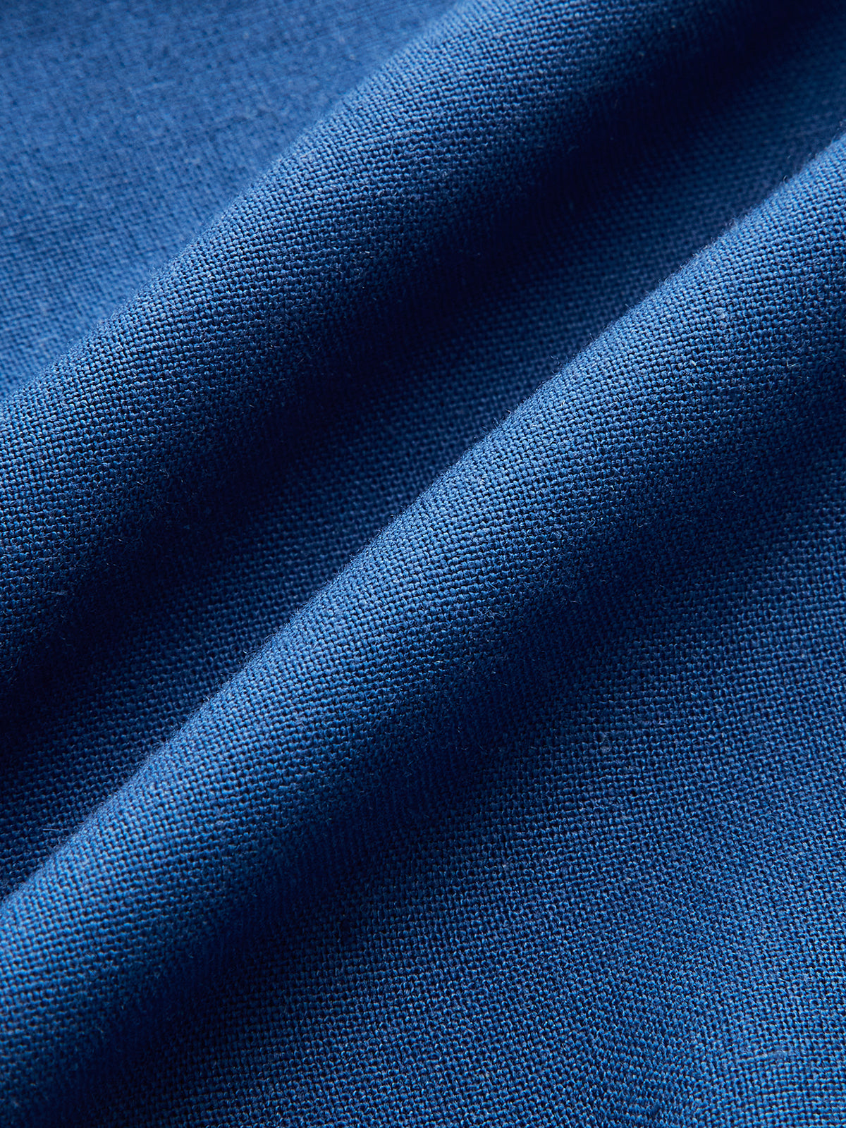 Blue beaded asymmetric sleeveless top with wrap-tie detail, detailed fabric weave visible.