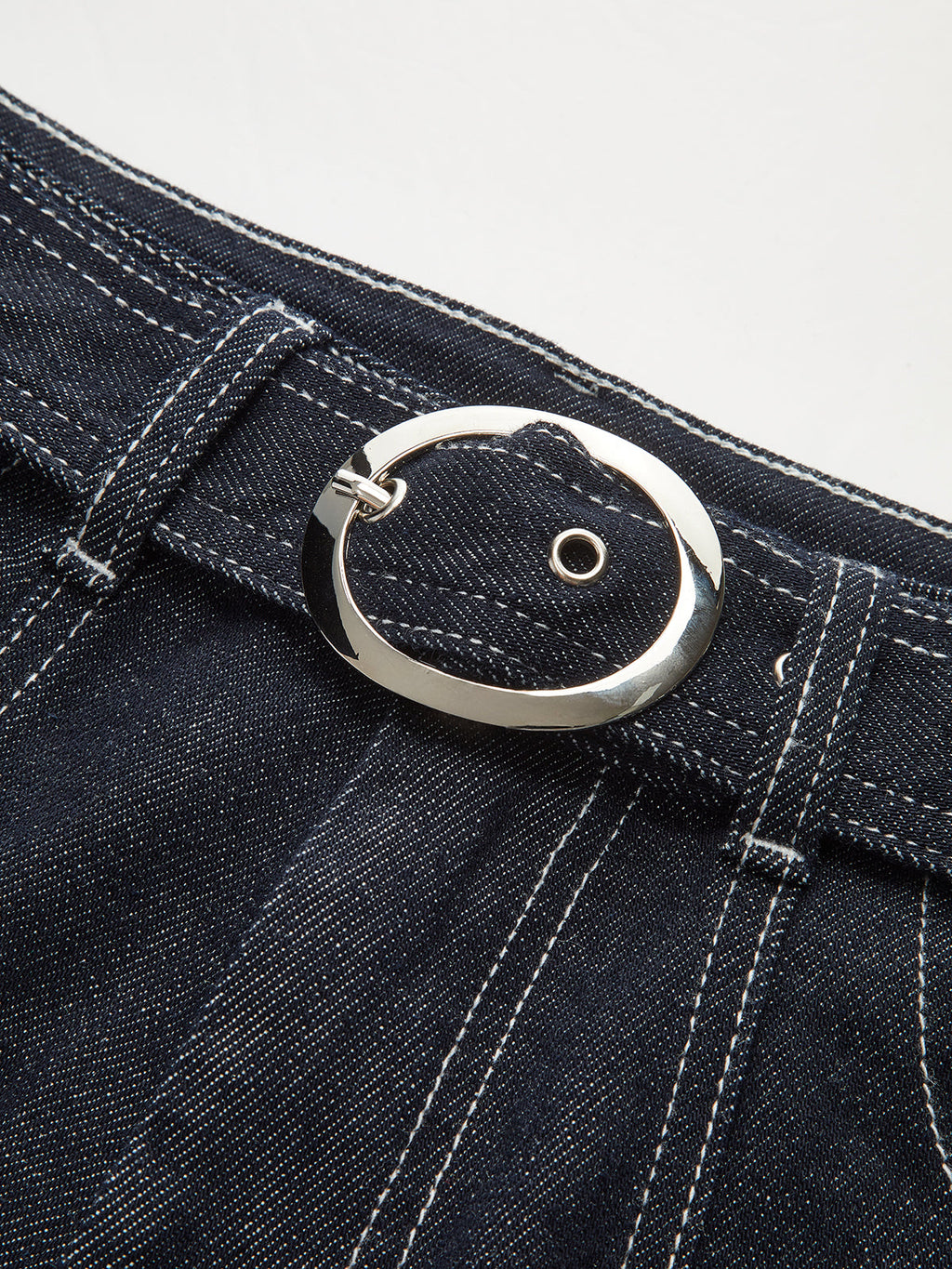 Denim trousers with white contrast stitching and a shiny silver oval buckle on the belt.