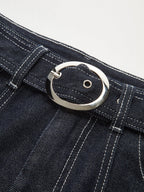 Denim trousers with white contrast stitching and a shiny silver oval buckle on the belt.