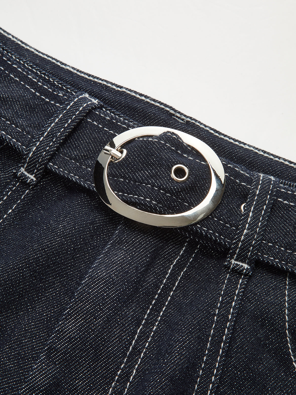 Denim trousers with white contrast stitching and a shiny silver oval buckle on the belt.