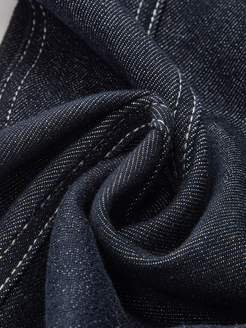 Dark indigo denim trousers with white contrast stitching, twill weave, and subtle slub texture.
