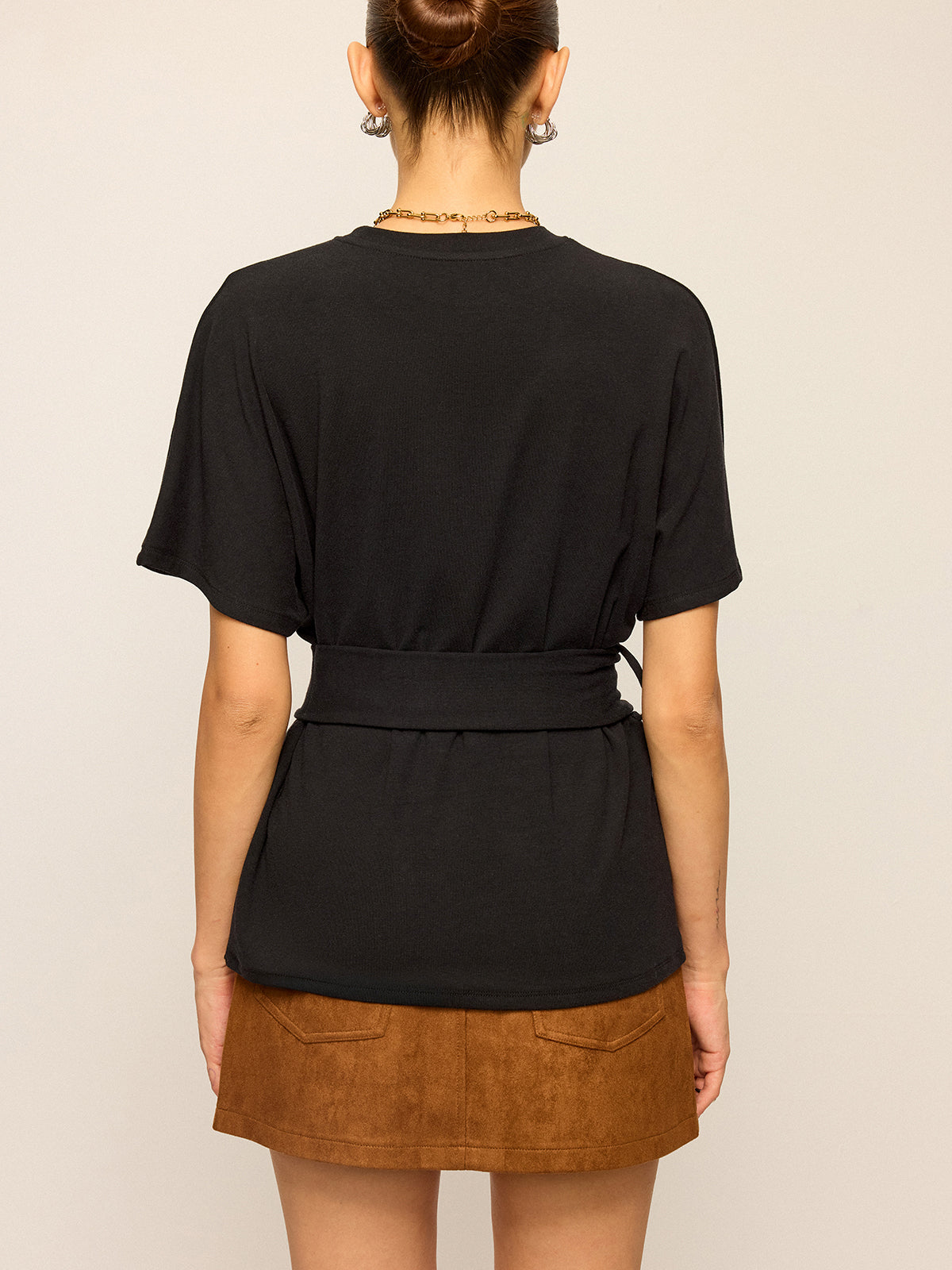Short-sleeve top with belt detail paired with a brown suede mini skirt featuring back pockets.