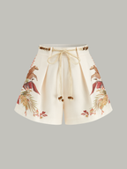 Cream mid-waist shorts with pleats, tropical beaded rope belt, and earthy floral print.