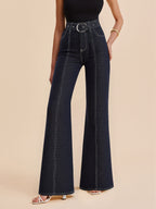 High-waisted dark blue denim trousers with contrast stitching and a belted waist, paired with a black sleeveless top.