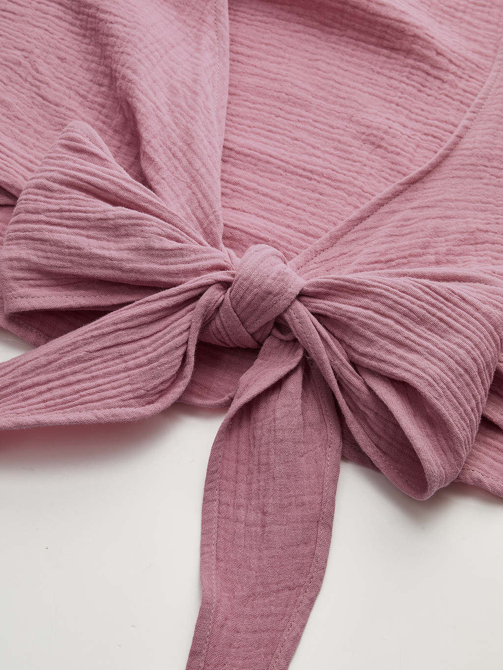 Dusty pink cropped tie-front blouse with long sleeves, textured cotton ridges, and a neat bow.