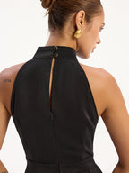 Sleeveless satin halter neck jumpsuit with back slit and two button closures at neck.