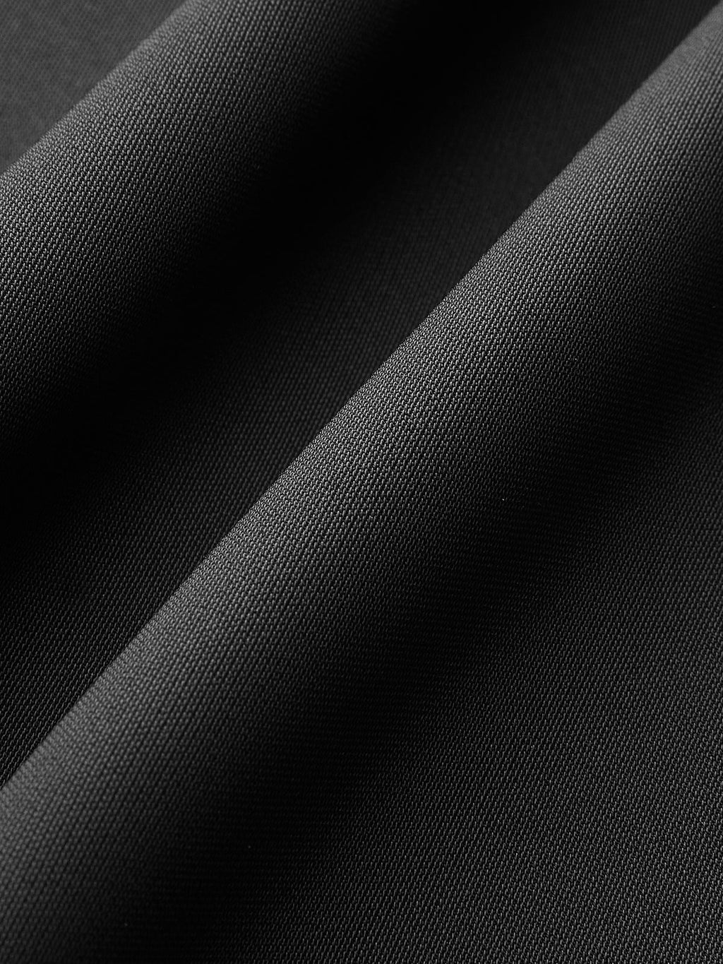 Close-up of black jumpsuit’s fine, textured weave, with soft folds, shadows, and highlights.