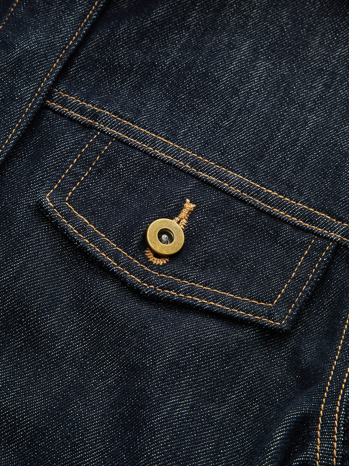 Dark blue cropped denim top with yellow stitching, pointed flap pocket, brass-tone button.