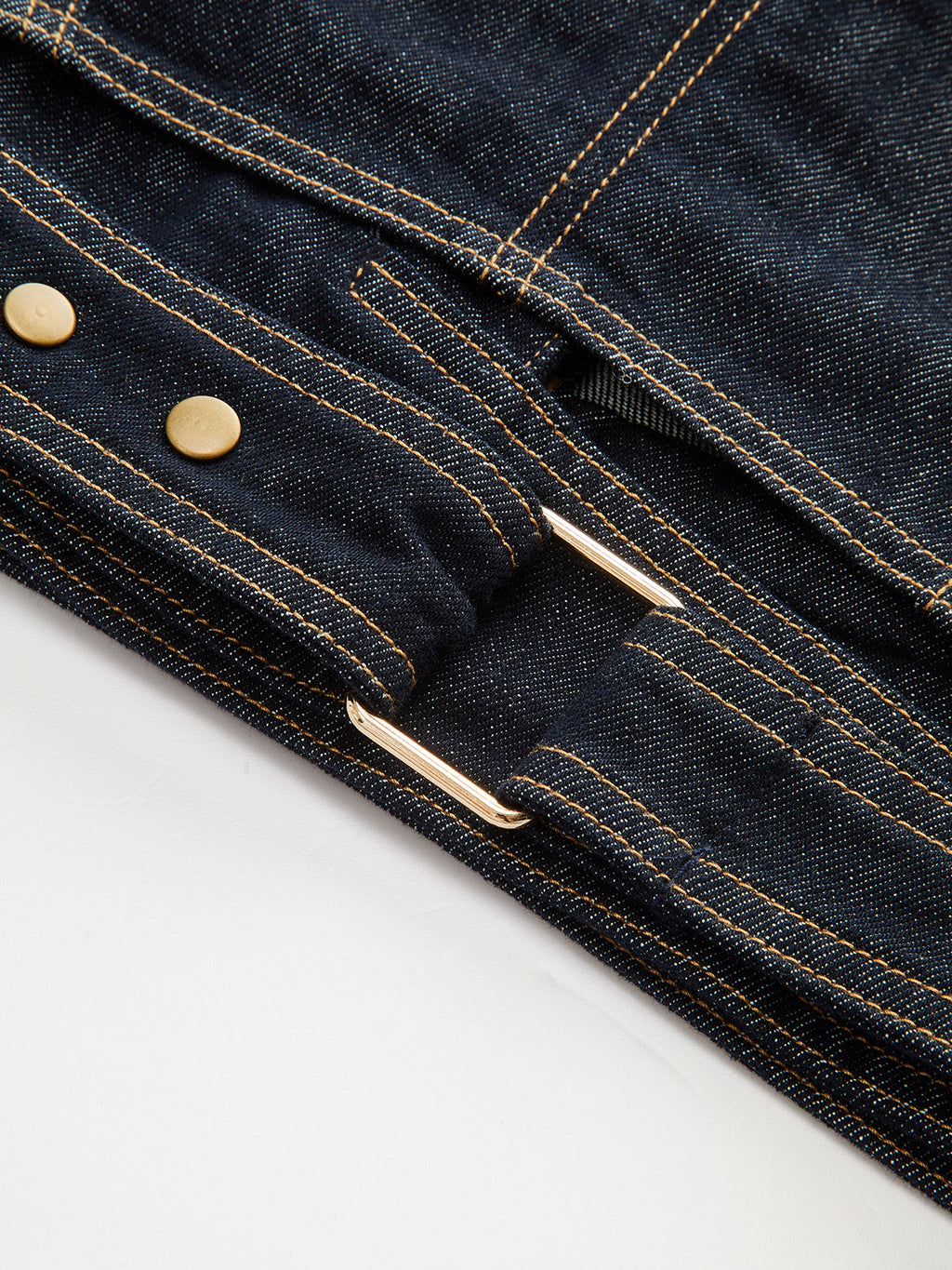 Cropped denim top with short sleeves, dark blue fabric, yellow stitching, brass buttons, metal buckle.